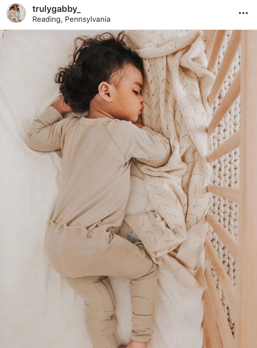 A toddler sleeps peacefully on a Diamond Cashmere Baby Blanket by Nivas, nestled in a crib.