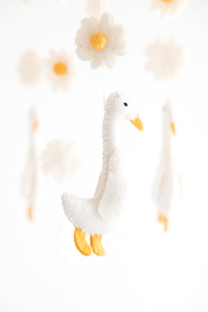 The Nivas Duck Crib Mobile, featuring handmade elements with white felt geese, flowers, and yellow accents, adds charming nursery décor against a crisp white background.