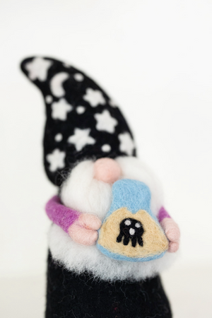 The Nivas Halloween Gnome - Wizard features a handmade design with a black star-and-moon hat and holds a blue object with a black-and-white spider—ideal for whimsical Halloween décor.