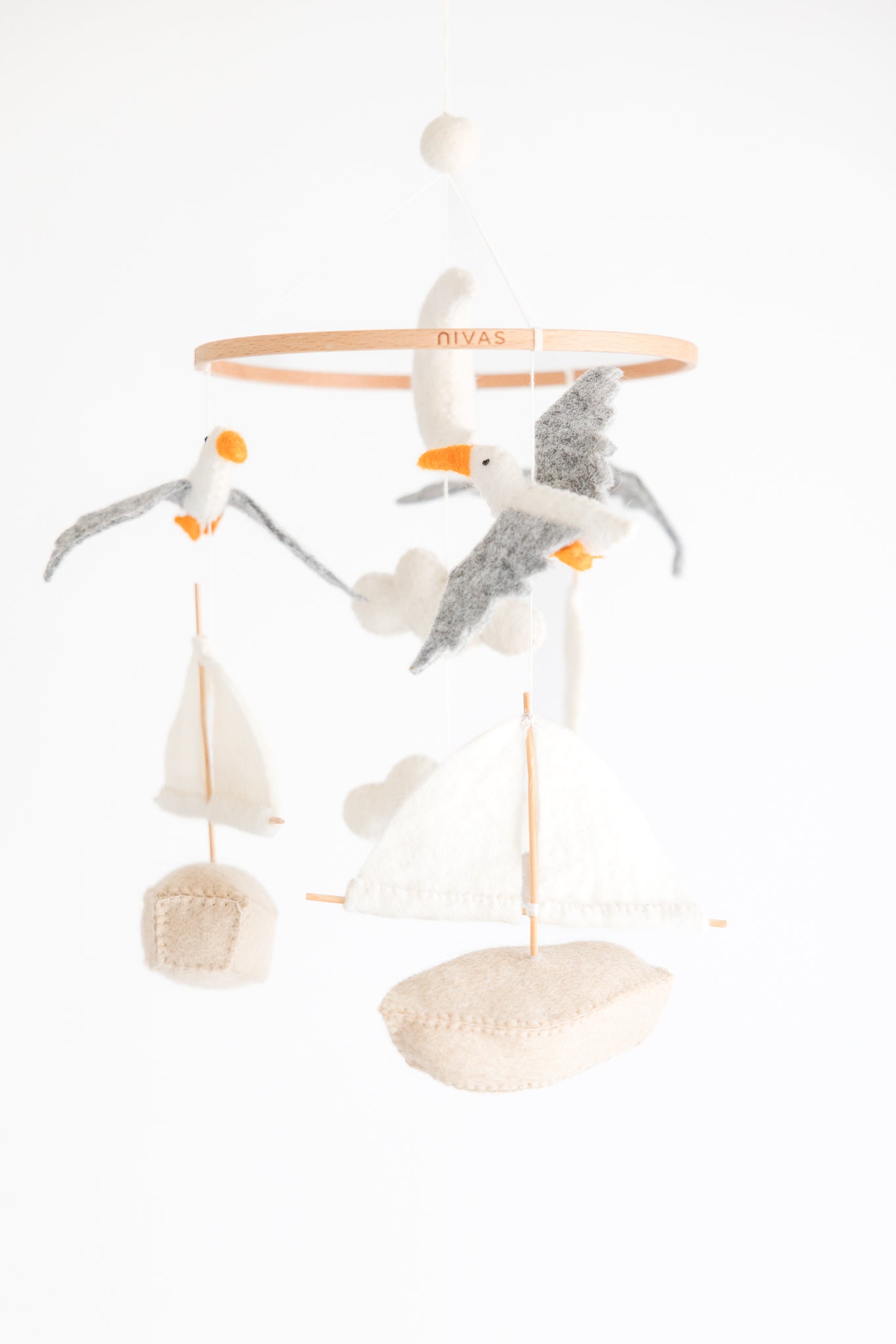 The Sailboat & Seagull Crib Mobile by Nivas features a nautical theme with felt sailboats, seagulls, and clouds on a wooden ring. It makes a charming baby shower gift and stands out beautifully against a plain white background.