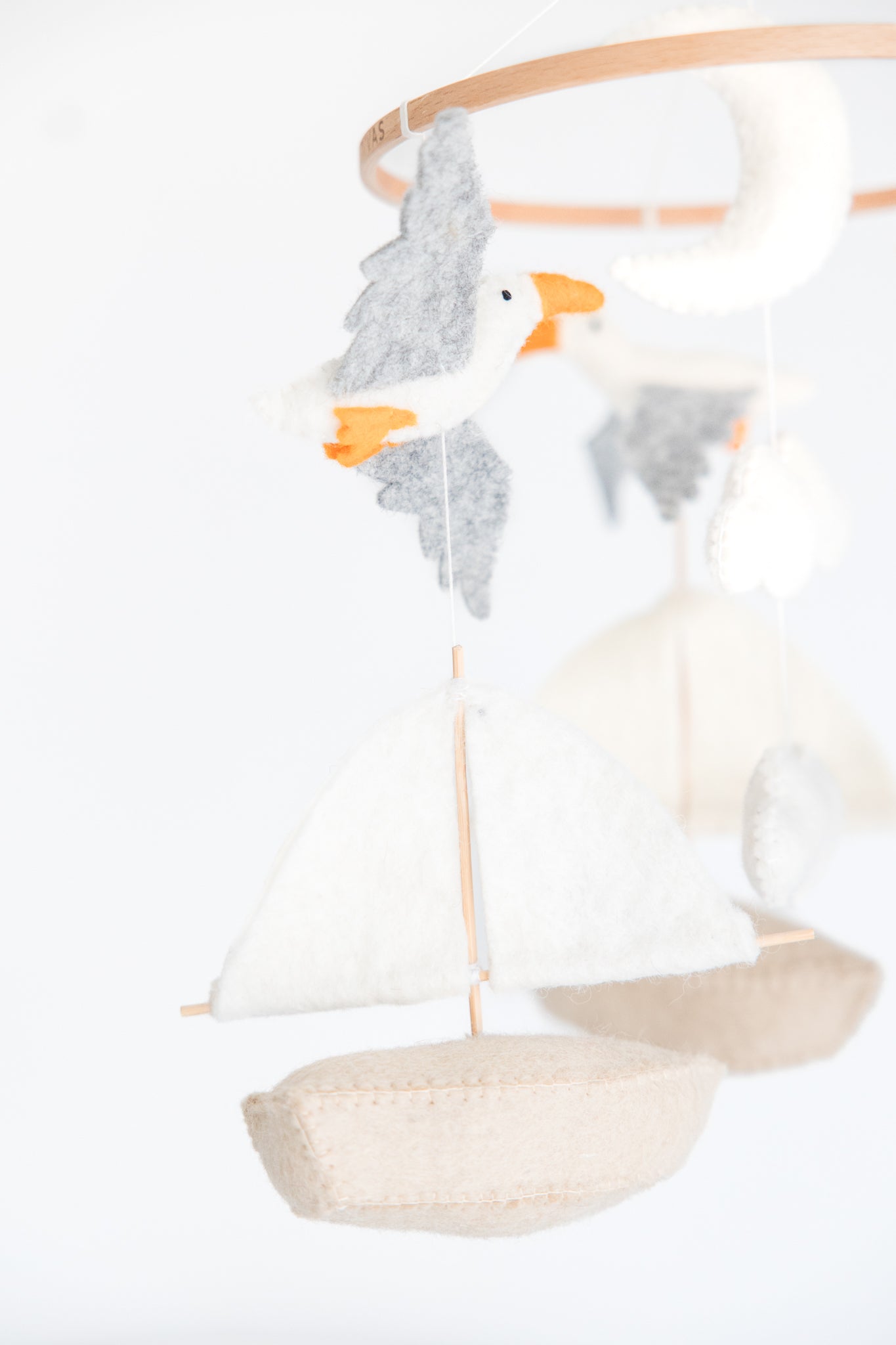 The Nivas Sailboat & Seagull Crib Mobile features a nautical theme with felt sea elements like a gray and white seagull and beige sailboat against a white background, making it an ideal baby shower gift.