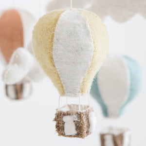 Felt hot air balloon ornaments in pastel colors, including yellow, pink, and blue, with small baskets attached, hanging against a light background.