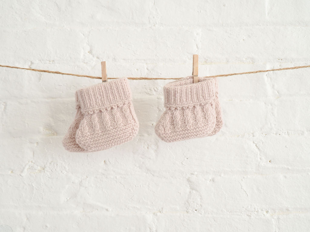 Nivas Collection, Cashmere baby booties, baby booties hung on string, White brick wall, cashmere baby socks